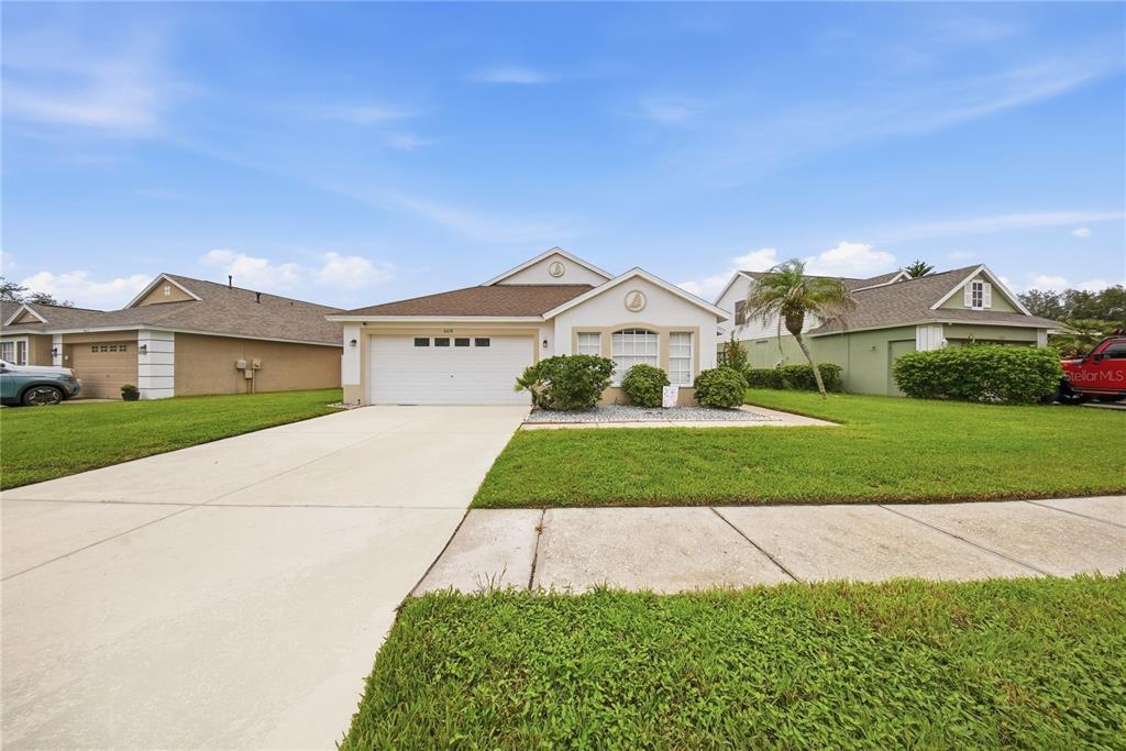 A single-story suburban house with a two-car garage, beige stucco exterior, and a green lawn — 6618 SUMMER COVE DRIVE, RIVERVIEW, FL
