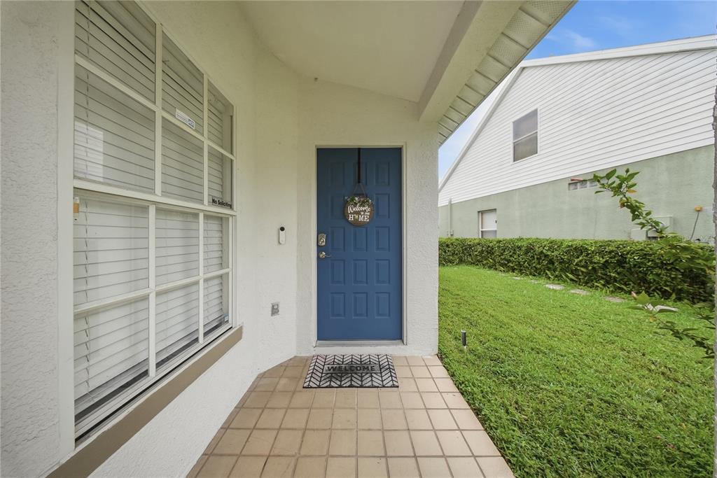 A blue front door with a welcome sign sits on a tiled porch next to a window — 6618 SUMMER COVE DRIVE, RIVERVIEW, FL