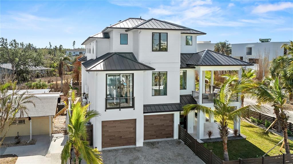 A three-story white house with a dark metal roof and two wood-paneled garage doors — 7007 POINT OF ROCKS ROAD, SARASOTA, FL