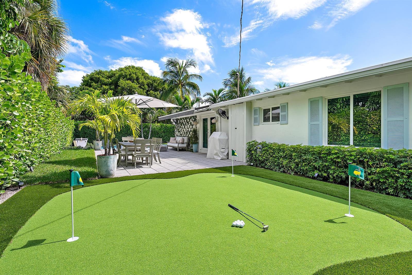 A backyard features a putting green with two flags, a patio dining area, and landscaping — 8001 Arlington Place, West Palm Beach FL 33405, WEST PALM BEACH, FL