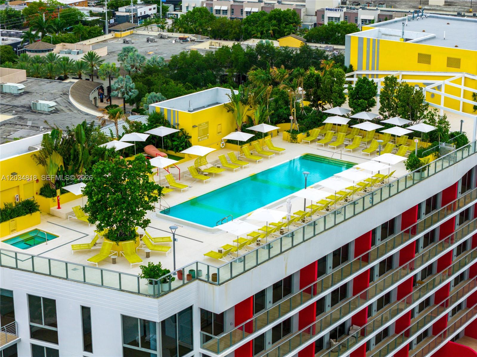An elevated outdoor swimming pool deck features yellow lounge chairs, umbrellas, and tropical landscaping — 90 NE 32 St # 203, Miami FL 33127, MIAMI, FL
