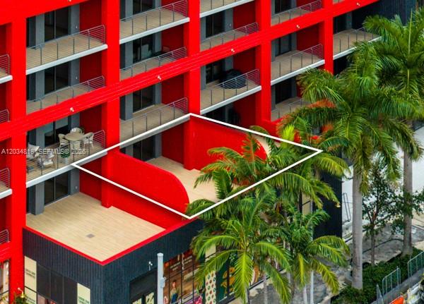 An exterior view of a red building featuring a large, open-air balcony with wood-look flooring — 90 NE 32 St # 203, Miami FL 33127, MIAMI, FL