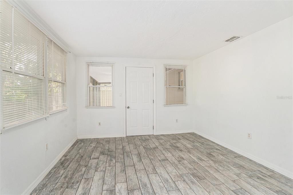 An empty room features white walls, gray wood-look tile flooring, and three windows with blinds — 3036 BLUE BIRD DRIVE, HOLIDAY, FL