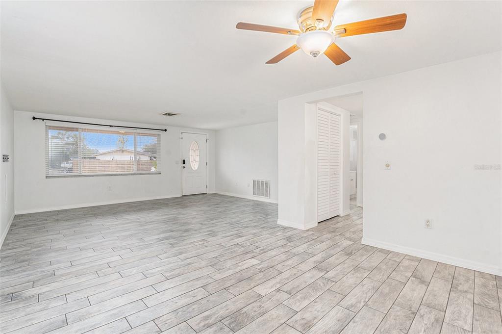 A bright living room features light gray wood-look tile flooring, white walls, and a ceiling fan — 3036 BLUE BIRD DRIVE, HOLIDAY, FL