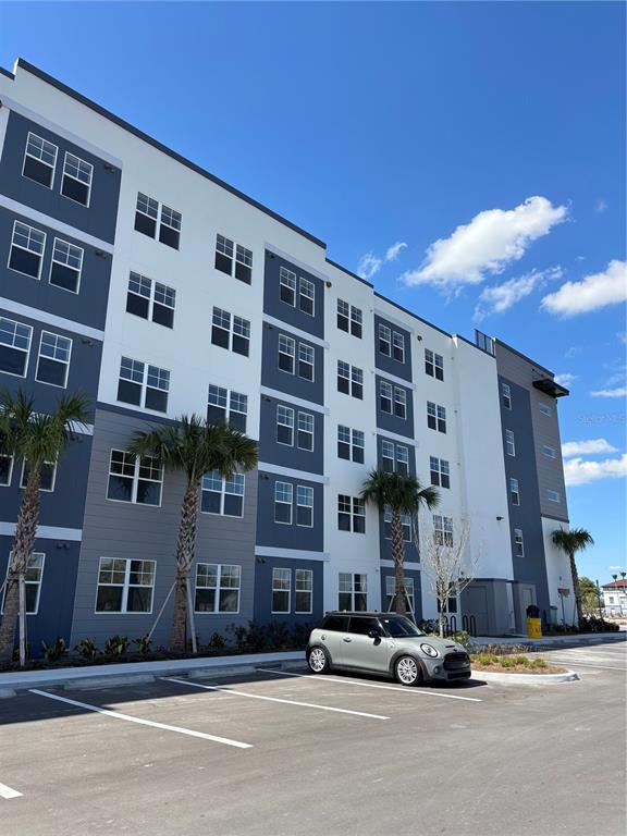 A multi-story apartment building stands next to a grassy lawn and a small pond — 5579 MILLENIA PARK UNIT 517, ORLANDO, FL