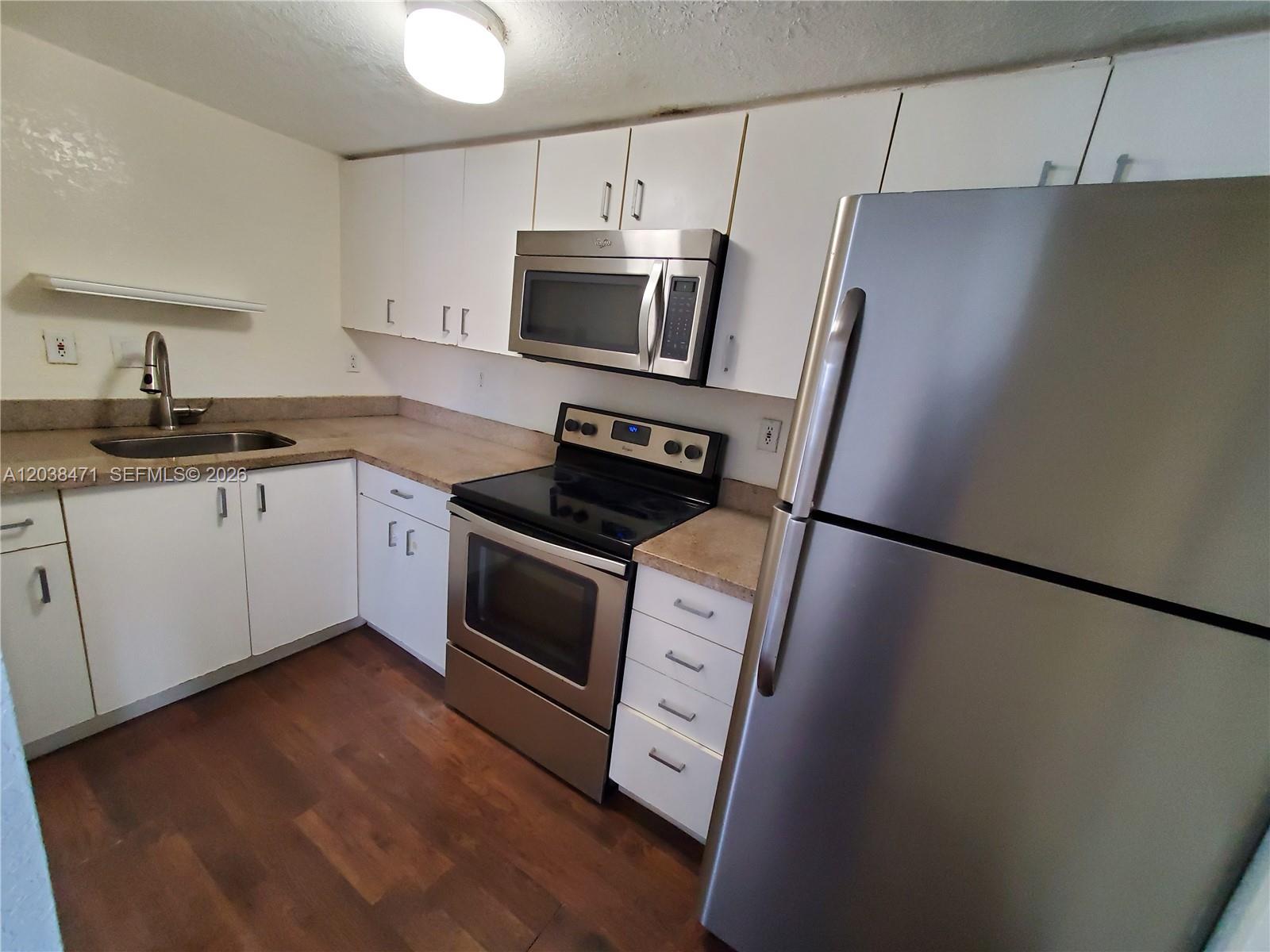 A kitchen features white cabinets, stainless steel appliances, a sink, and wood-look flooring — 300 NW 84th Ter # 300, Miami FL 33150, MIAMI, FL