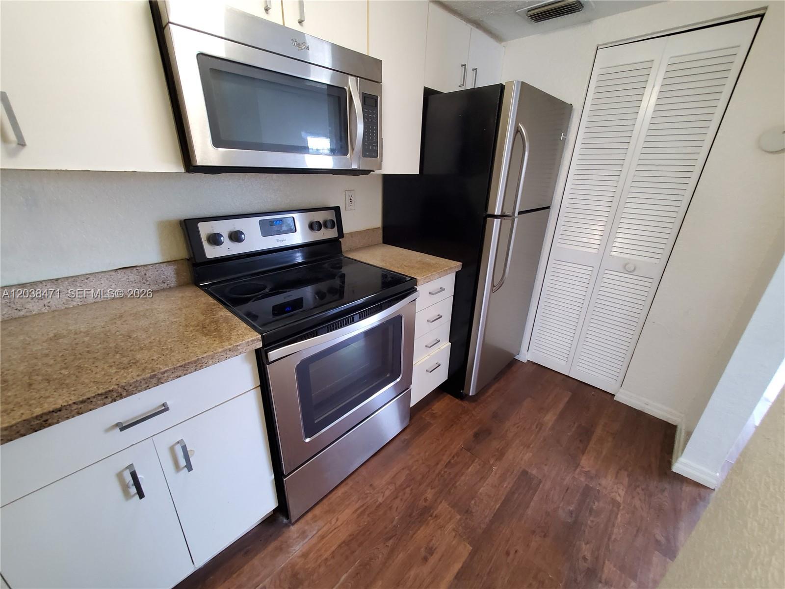 A kitchen features white cabinets, stainless steel appliances, a black stove, and wood-look flooring — 300 NW 84th Ter # 300, Miami FL 33150, MIAMI, FL