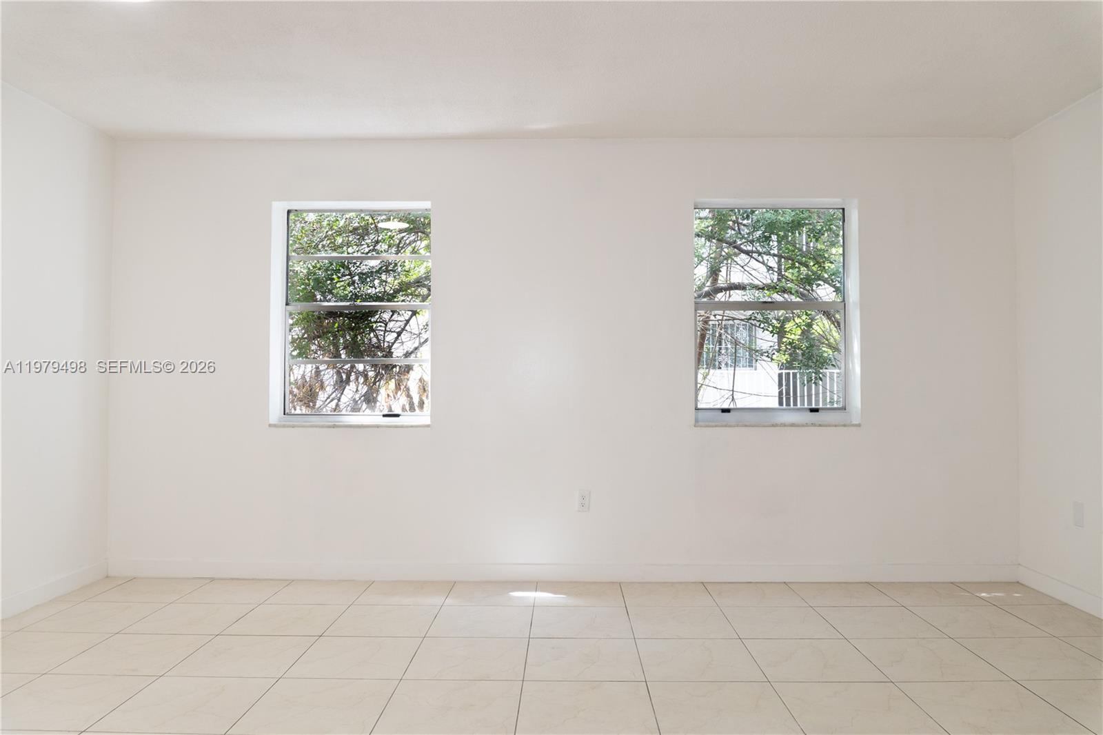 A room with white walls, light-colored tile flooring, and two windows looking out at trees — 1525 NW 19th Ter # 15, Miami FL 33125, MIAMI, FL