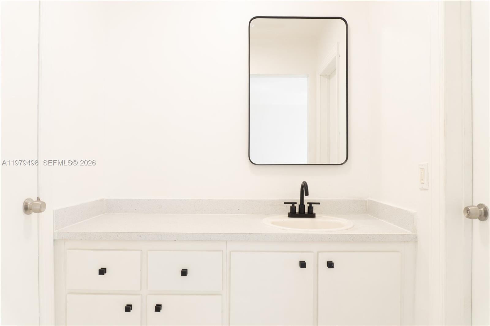 A bathroom vanity features a white countertop, black faucet, and a rectangular mirror — 1525 NW 19th Ter # 15, Miami FL 33125, MIAMI, FL