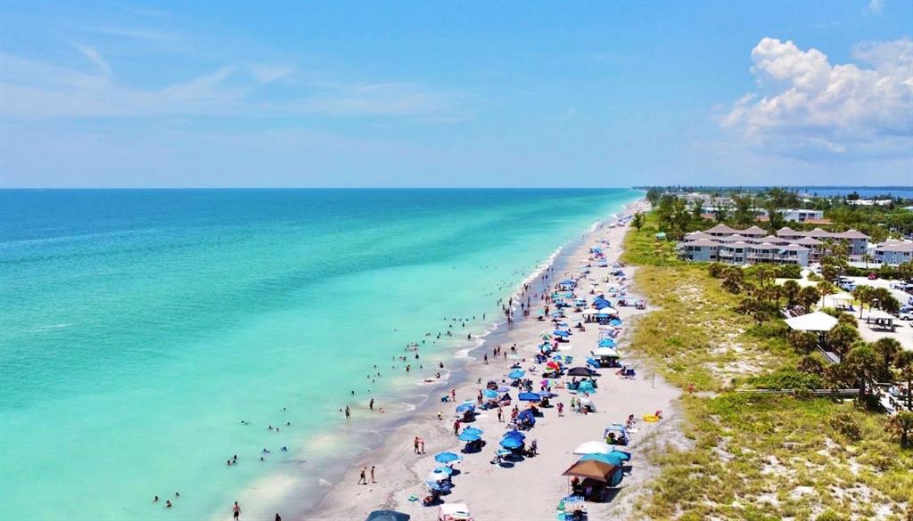 An aerial view shows a sandy beach with many umbrellas and people along the oceanfront — 21471 QUESADA AVENUE, PORT CHARLOTTE, FL
