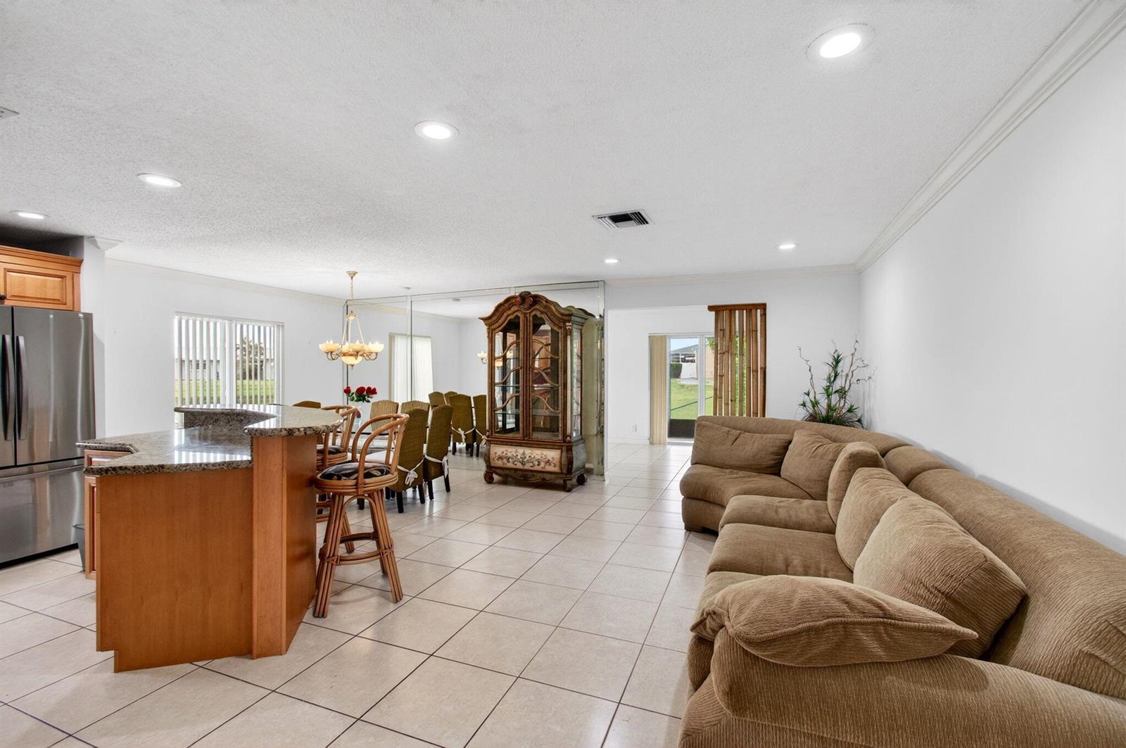 An open-concept living and dining area features tile flooring, a kitchen island, and a sofa — 6049 Dusenburg Road, Delray Beach FL 33484, DELRAY BEACH, FL