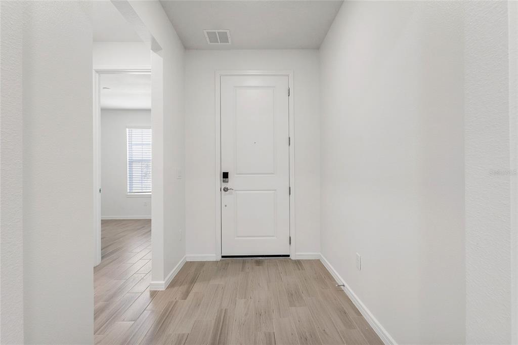 A bright entryway features white walls, light wood-look flooring, and a central white front door — 6376 SHIMMERING SHORES LANE, ST CLOUD, FL