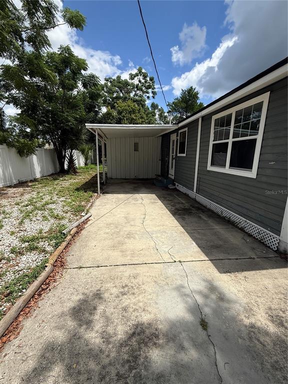 A concrete driveway leads to a covered carport beside a gray house with white trim — 137 E MAINE AVENUE, LONGWOOD, FL
