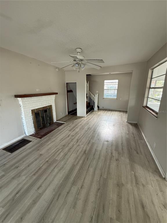 A living room features light wood-look flooring, a white brick fireplace, and a ceiling fan — 137 E MAINE AVENUE, LONGWOOD, FL