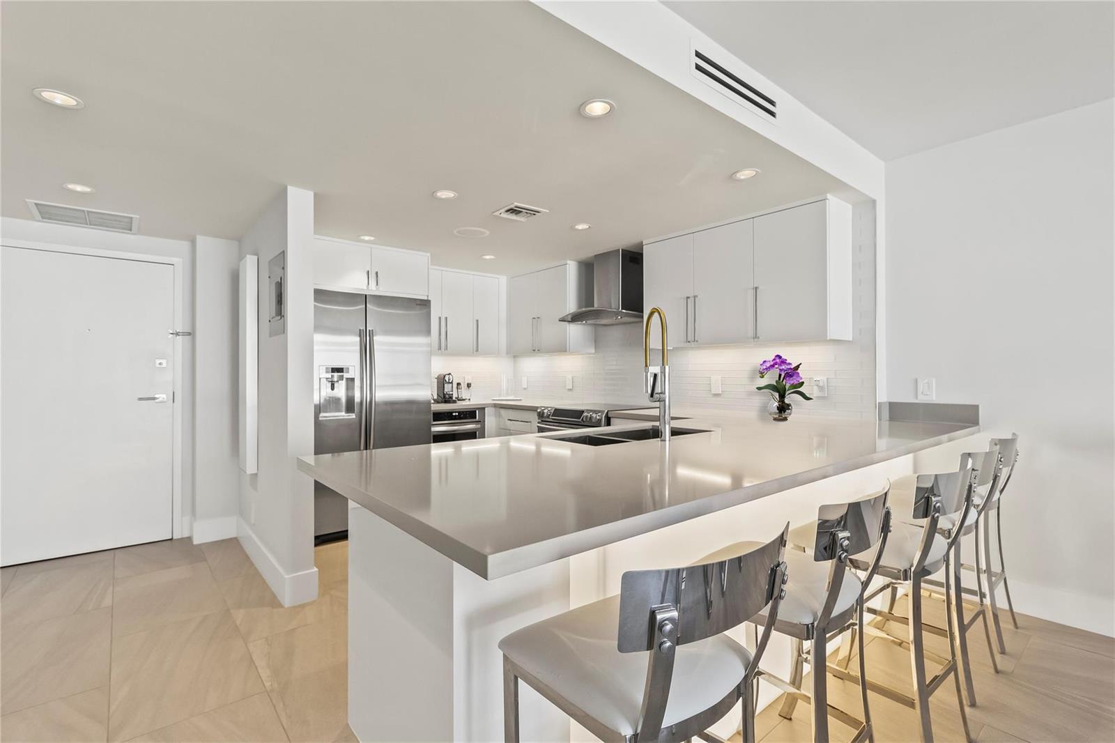 A modern kitchen features white cabinetry, stainless steel appliances, and a large quartz breakfast bar — 800 SE 20th Avenue # 809, Deerfield Beach FL 33441, DEERFIELD BEACH, FL