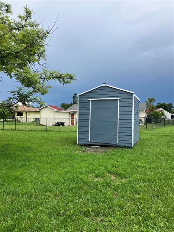 A blue metal storage shed sits in a grassy backyard behind a chain-link fence — 7570 BERWICK STREET, NORTH PORT, FL