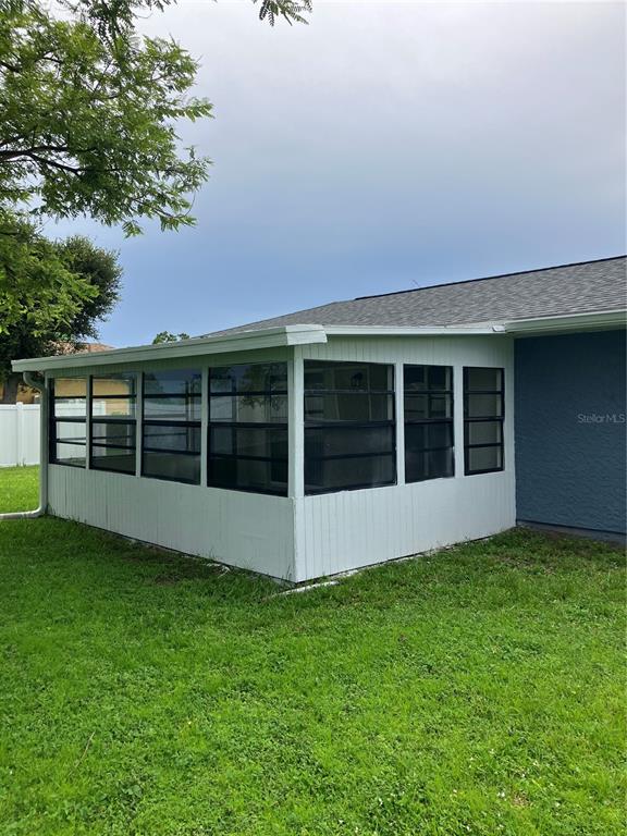 A white enclosed sunroom with black-framed windows sits on a grassy lawn beside a house — 7570 BERWICK STREET, NORTH PORT, FL