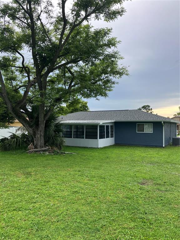 A blue house with a white screened-in porch stands behind a large tree — 7570 BERWICK STREET, NORTH PORT, FL
