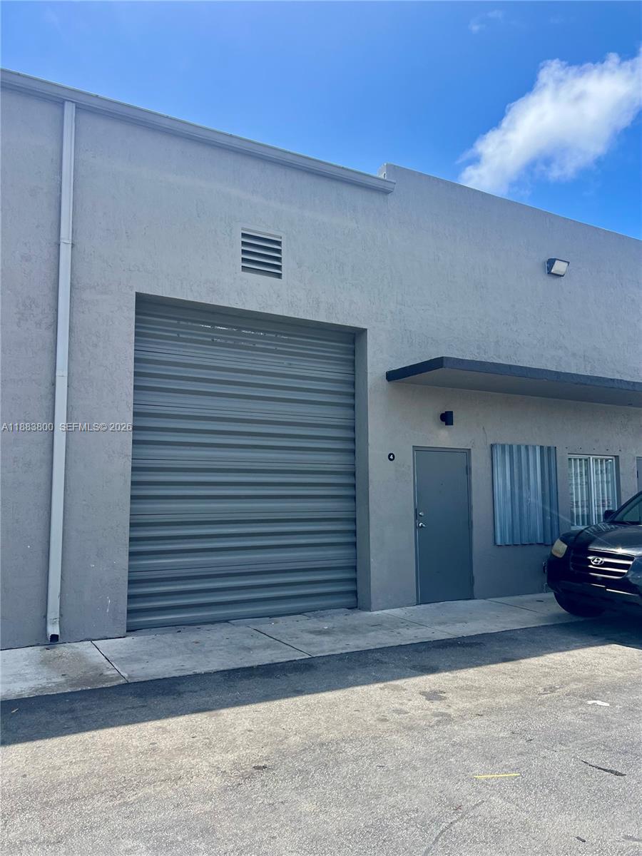 The exterior of a gray commercial warehouse building features a roll-up door and a pedestrian entrance — 16215 SW 117th Ave # 4, Miami FL 33177, MIAMI, FL