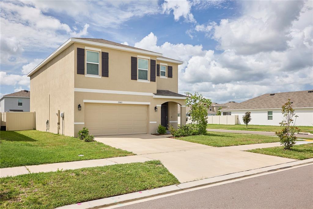 A two-story tan stucco house features a two-car garage and a small front porch — 33405 DARLEY DALE TRL, WESLEY CHAPEL, FL