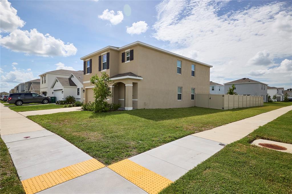 A two-story tan stucco house sits on a corner lot with a vinyl privacy fence — 33405 DARLEY DALE TRL, WESLEY CHAPEL, FL