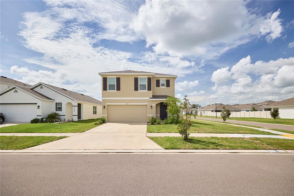 A two-story tan house with a two-car garage sits on a suburban street — 33405 DARLEY DALE TRL, WESLEY CHAPEL, FL