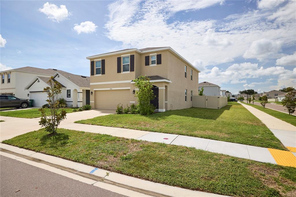 A two-story tan house with a two-car garage sits on a corner lot — 33405 DARLEY DALE TRL, WESLEY CHAPEL, FL