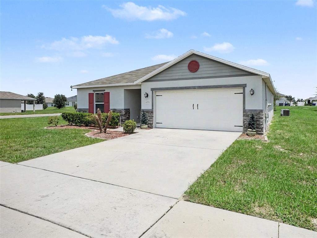A single-story suburban house features a two-car garage, stone accents, and red window shutters — 2488 BEGONIA STREET, MASCOTTE, FL