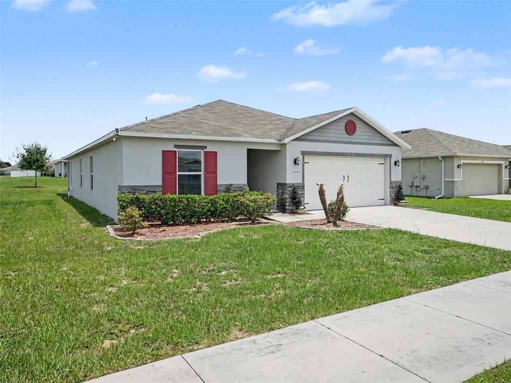 A single-story suburban house with a two-car garage, red shutters, and a landscaped front yard — 2488 BEGONIA STREET, MASCOTTE, FL