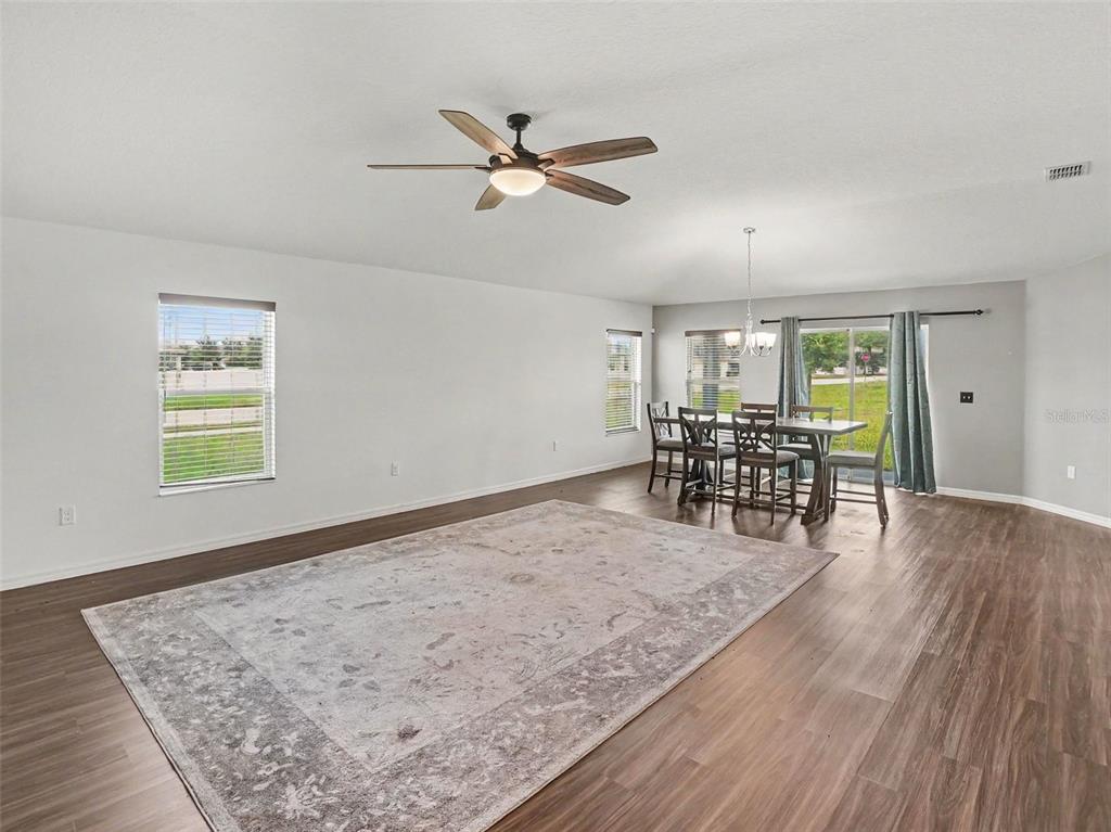A living and dining room with wood-look flooring, a ceiling fan, and neutral-toned furniture — 2488 BEGONIA STREET, MASCOTTE, FL