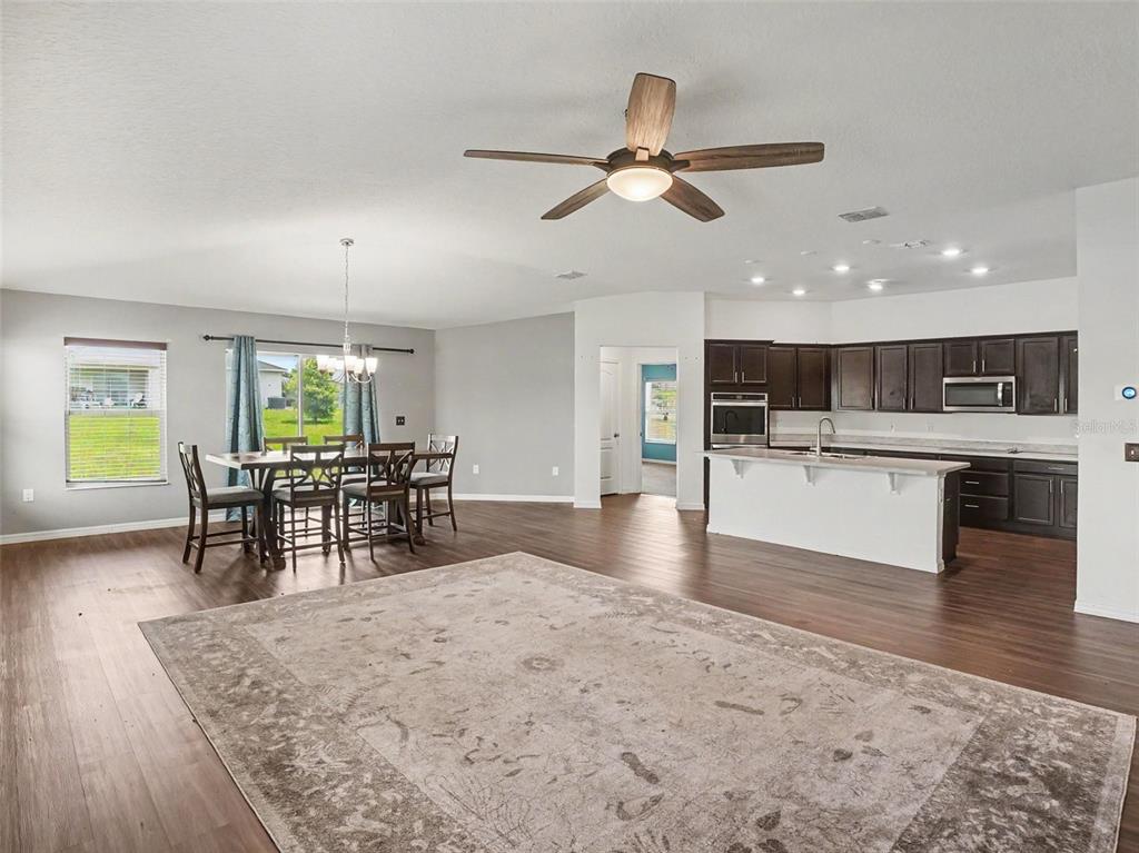 An open-concept living and dining area features wood-look flooring, a ceiling fan, and sliding doors — 2488 BEGONIA STREET, MASCOTTE, FL
