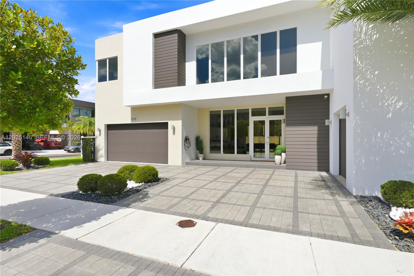 A modern two-story house features a paved driveway, a garage, and large glass windows — 7525 NW 103rd Pl, Doral FL 33178, DORAL, FL