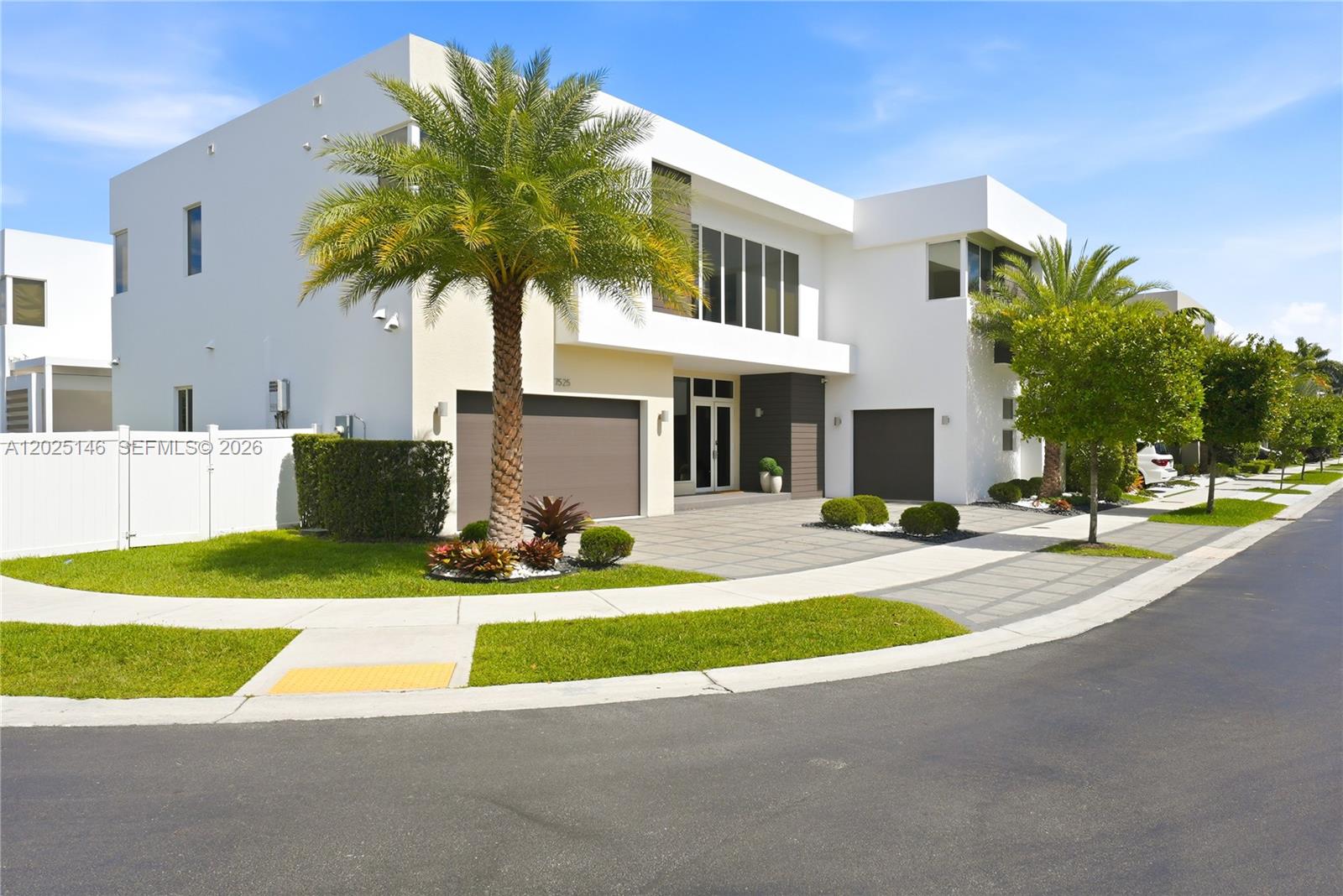 A modern two-story white house features a paved driveway, palm trees, and two garage doors — 7525 NW 103rd Pl, Doral FL 33178, DORAL, FL