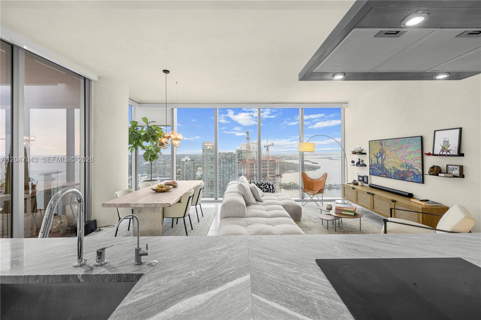 A modern open-concept living and dining area features floor-to-ceiling windows with expansive city and water views — 700 NE 26th Ter # 5006, Miami FL 33137, MIAMI, FL