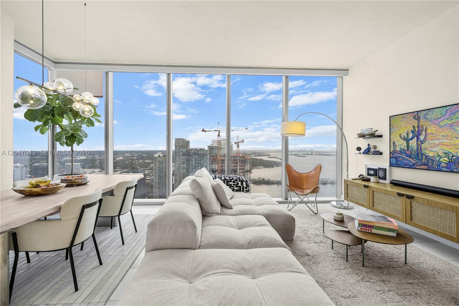 A modern living and dining area features floor-to-ceiling windows overlooking a city and bay — 700 NE 26th Ter # 5006, Miami FL 33137, MIAMI, FL