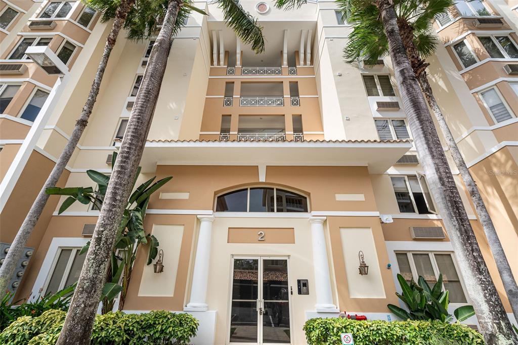 The exterior entrance of a multi-story tan apartment building features palm trees and glass doors — 1 PALMA REAL AVE. UNIT 2 A6, GUAYNABO, PR