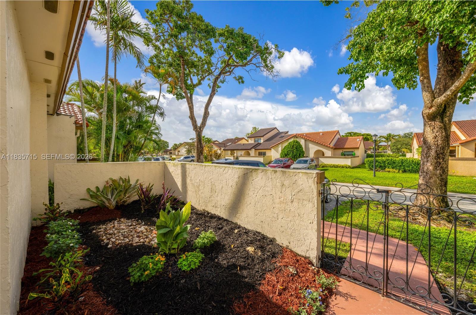 A small garden bed with mulch and plants sits beside a stucco wall and gate — 6637 NW 181st Ln, Hialeah FL 33015, HIALEAH, FL