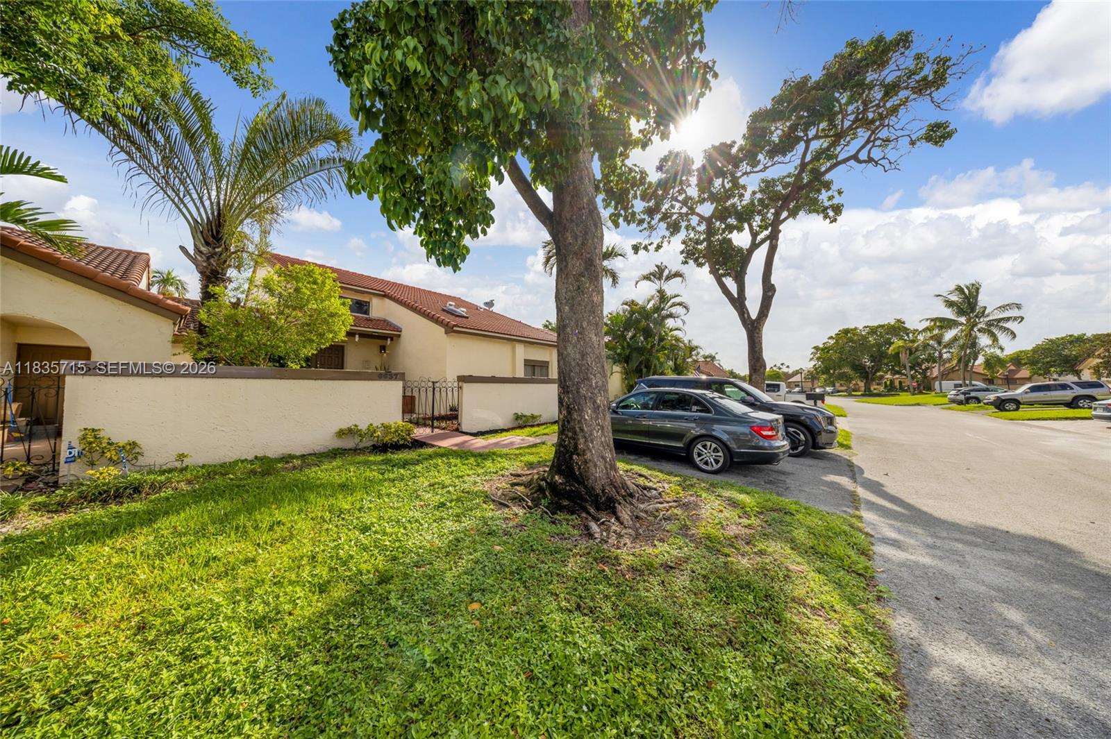A beige house with a tile roof sits behind a low wall near a large tree — 6637 NW 181st Ln, Hialeah FL 33015, HIALEAH, FL