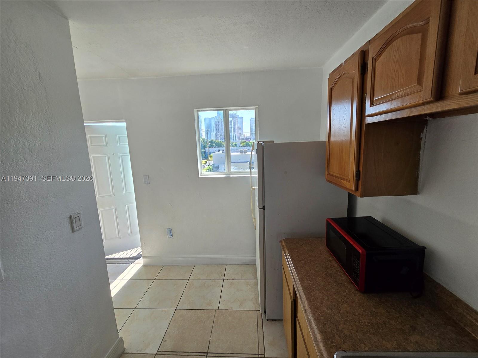 A kitchen features light tile flooring, wood cabinets, a white refrigerator, and a microwave — 535 NW 7th St # 10, Miami FL 33136, MIAMI, FL