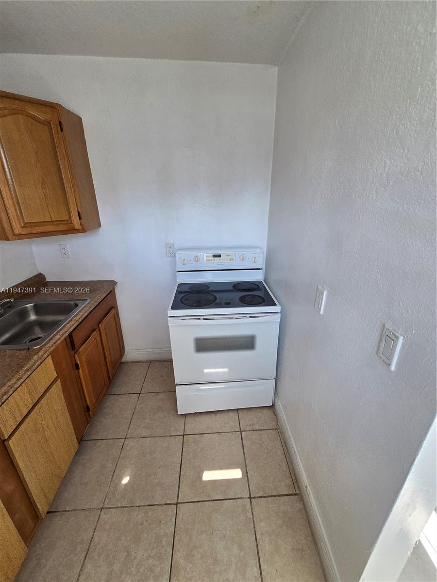 A kitchen features a white electric stove, wooden cabinets, and beige tile flooring — 535 NW 7th St # 10, Miami FL 33136, MIAMI, FL