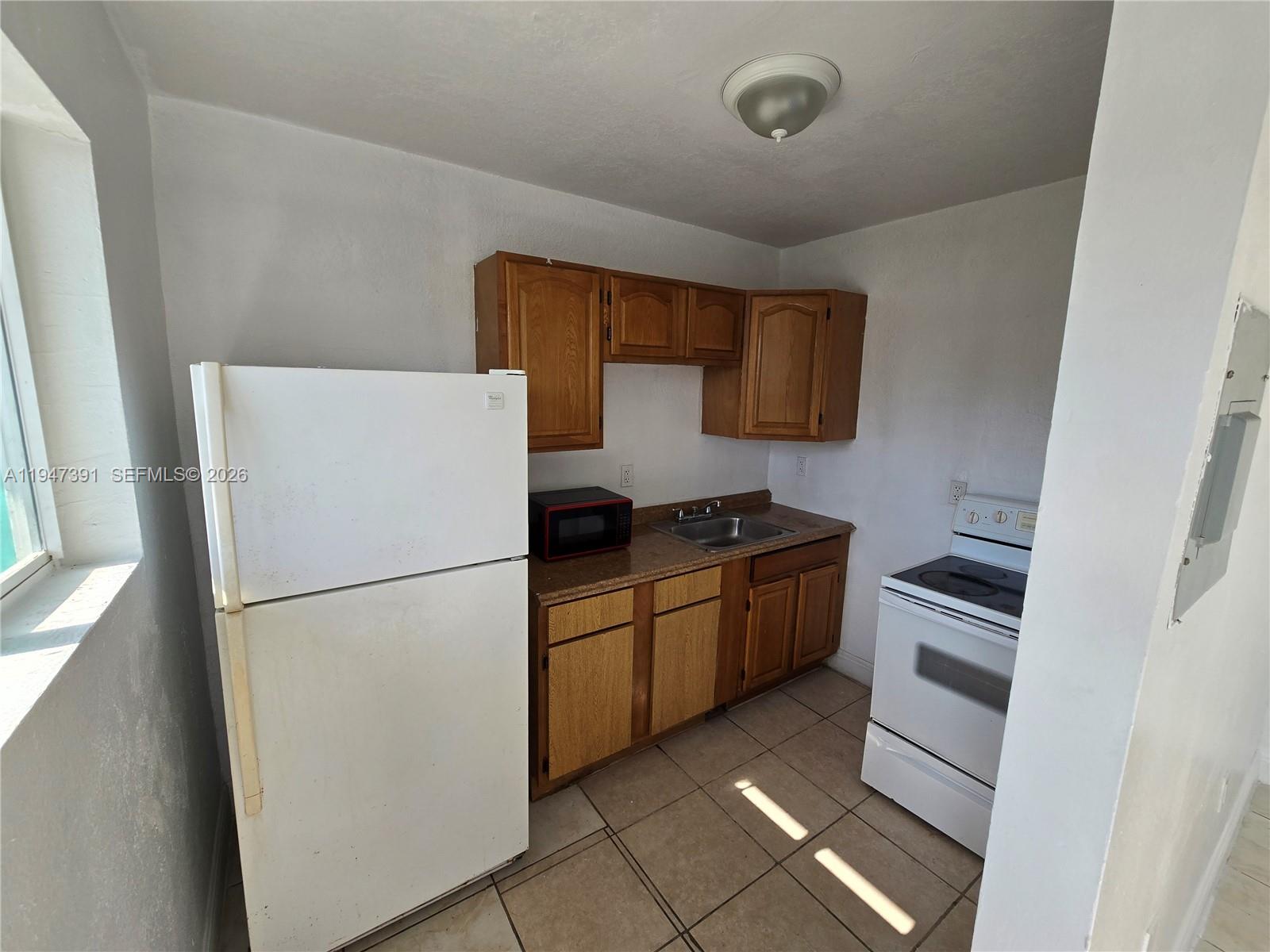 A small kitchen features white appliances, wood cabinets, a sink, and light-colored floor tiles — 535 NW 7th St # 10, Miami FL 33136, MIAMI, FL