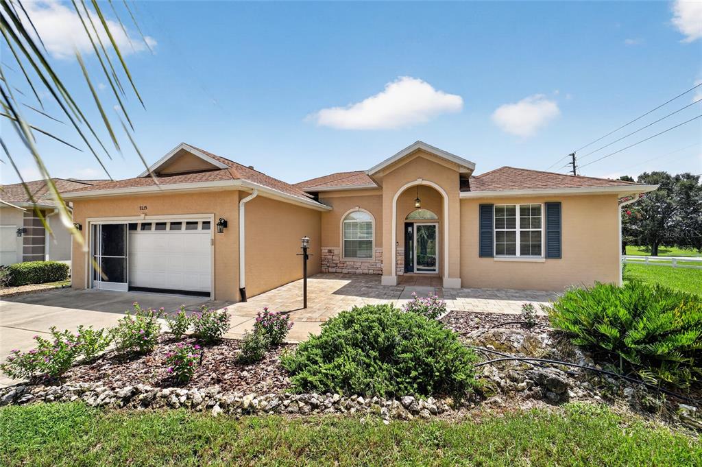A single-story house with a tan stucco exterior, a paved driveway, and a front lawn — 9275 SW 99TH COURT ROAD, OCALA, FL