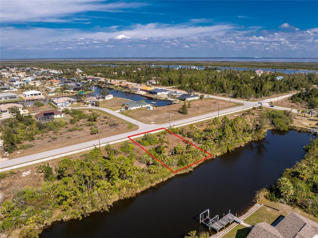 An aerial view shows a vacant, rectangular waterfront lot outlined in red next to a road — 15125 INGRAHAM BOULEVARD, PORT CHARLOTTE, FL