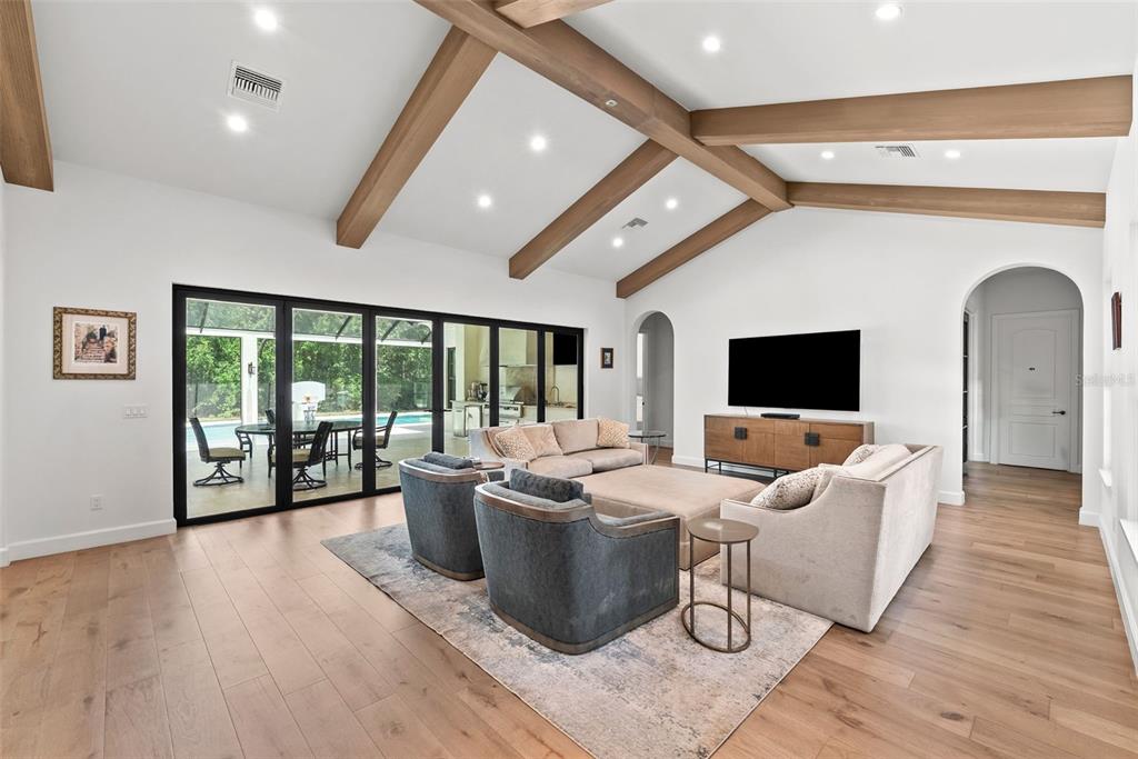 A spacious living room features vaulted ceilings with exposed wooden beams, hardwood floors, and glass doors — 18907 LAKES EDGE WAY, ODESSA, FL