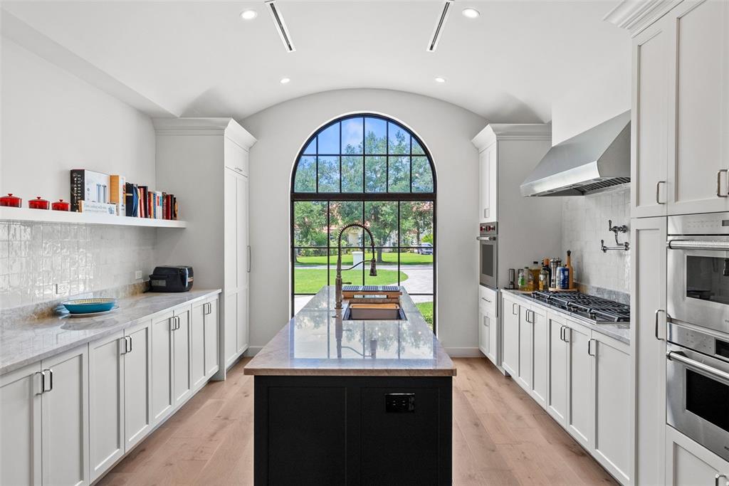 A kitchen features white cabinetry, a dark central island, and a large arched window — 18907 LAKES EDGE WAY, ODESSA, FL