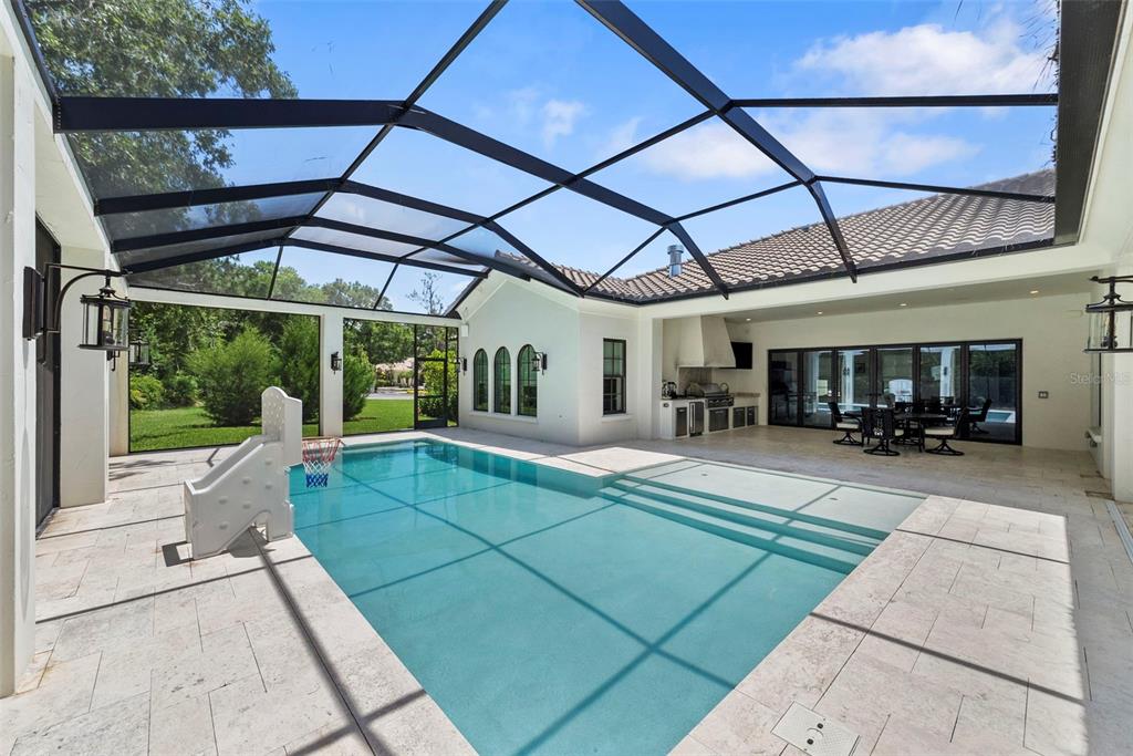A screened-in patio features a rectangular swimming pool, a slide, and an outdoor kitchen area — 18907 LAKES EDGE WAY, ODESSA, FL
