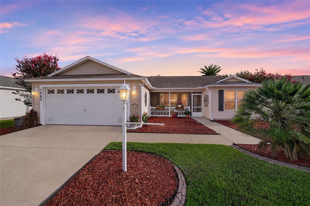 A single-story house with a white garage, a front porch, and a landscaped yard at sunset — 1563 HOLLYBERRY PLACE, THE VILLAGES, FL