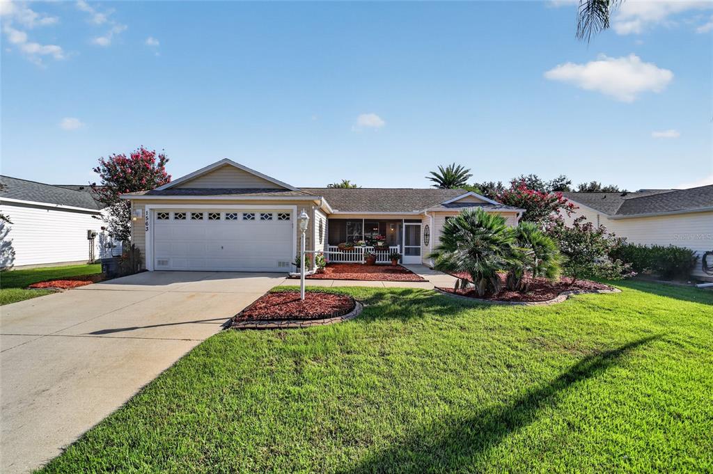 A single-story house with a two-car garage, a screened front porch, and a landscaped lawn — 1563 HOLLYBERRY PLACE, THE VILLAGES, FL