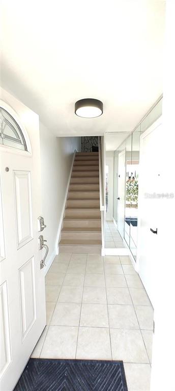 A tiled entryway features a white front door, a staircase, and a mirrored wall — 255 CAPRI CIRCLE N UNIT 36, TREASURE ISLAND, FL