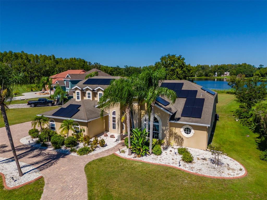 An aerial view of a tan house with solar panels on the roof near a lake — 2327 CAMP INDIANHEAD ROAD, LAND O LAKES, FL